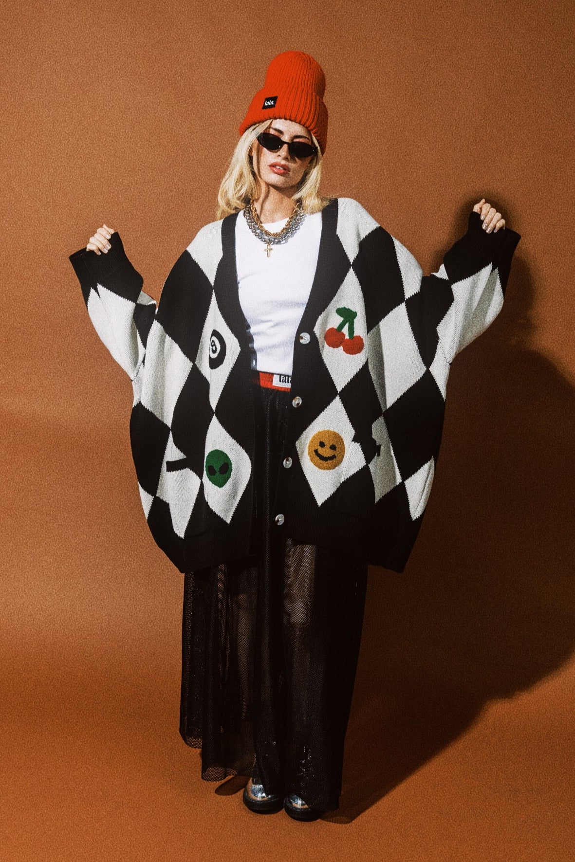 Person wearing a black and white checkered cardigan with colorful designs on an orange background