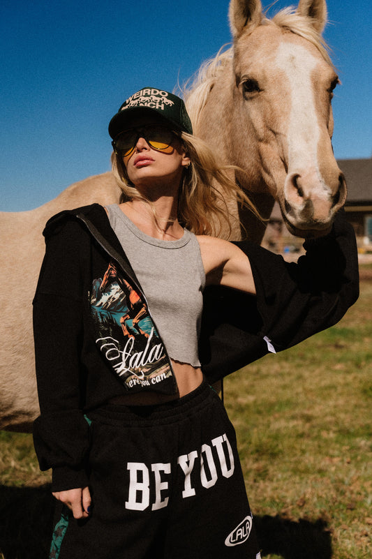 Person standing in a field wearing a sweatsuit with a horse