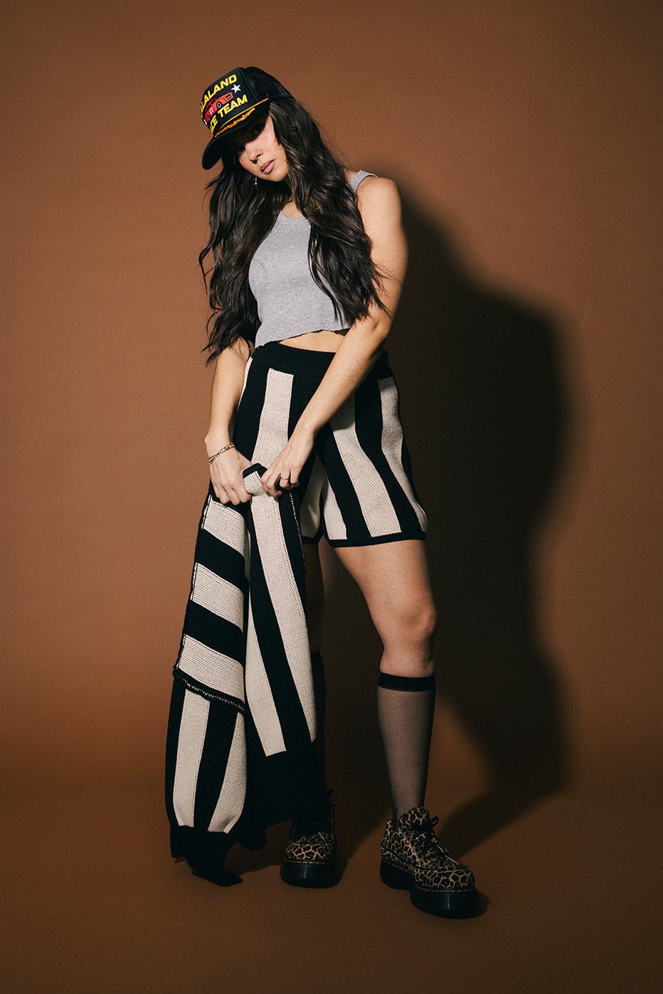 Person wearing a black and white striped set, gray top, and black shoes against a brown background