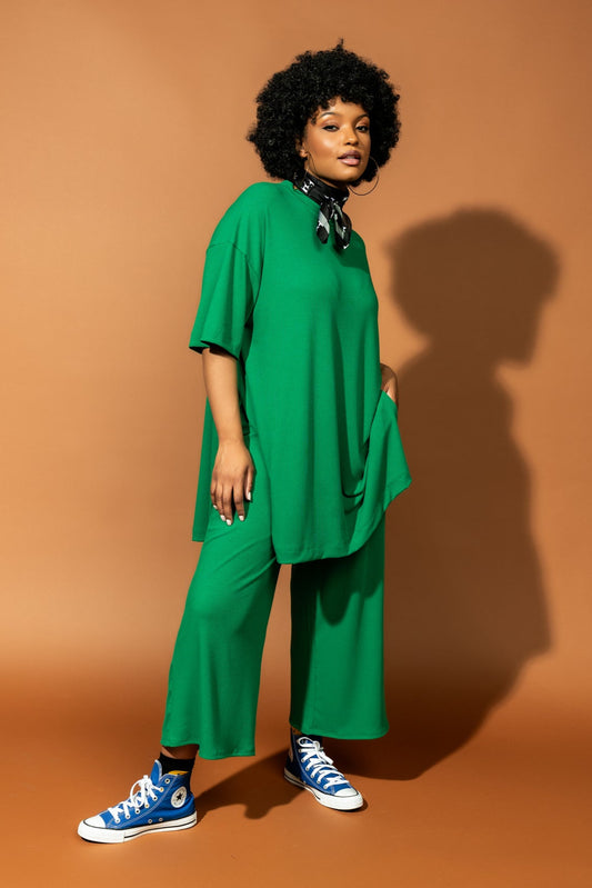 photo of girl wearing green ribbed matching set. The top is long and oversized with high side slits. Pants are cropped and wide leg with an elastic waistband.