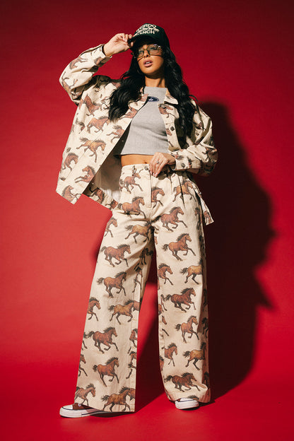 Person wearing white denim wide leg trousers with a horse pattern on a red background