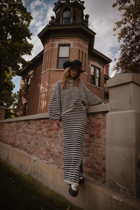 Person in a striped sweater and skirt with fuzzy texture standing against a brick wall.