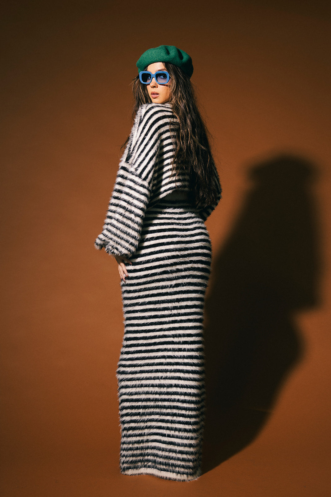 Woman wearing a black and white stripe sweater and maxi skirt with fuzzy texture against a brown background.