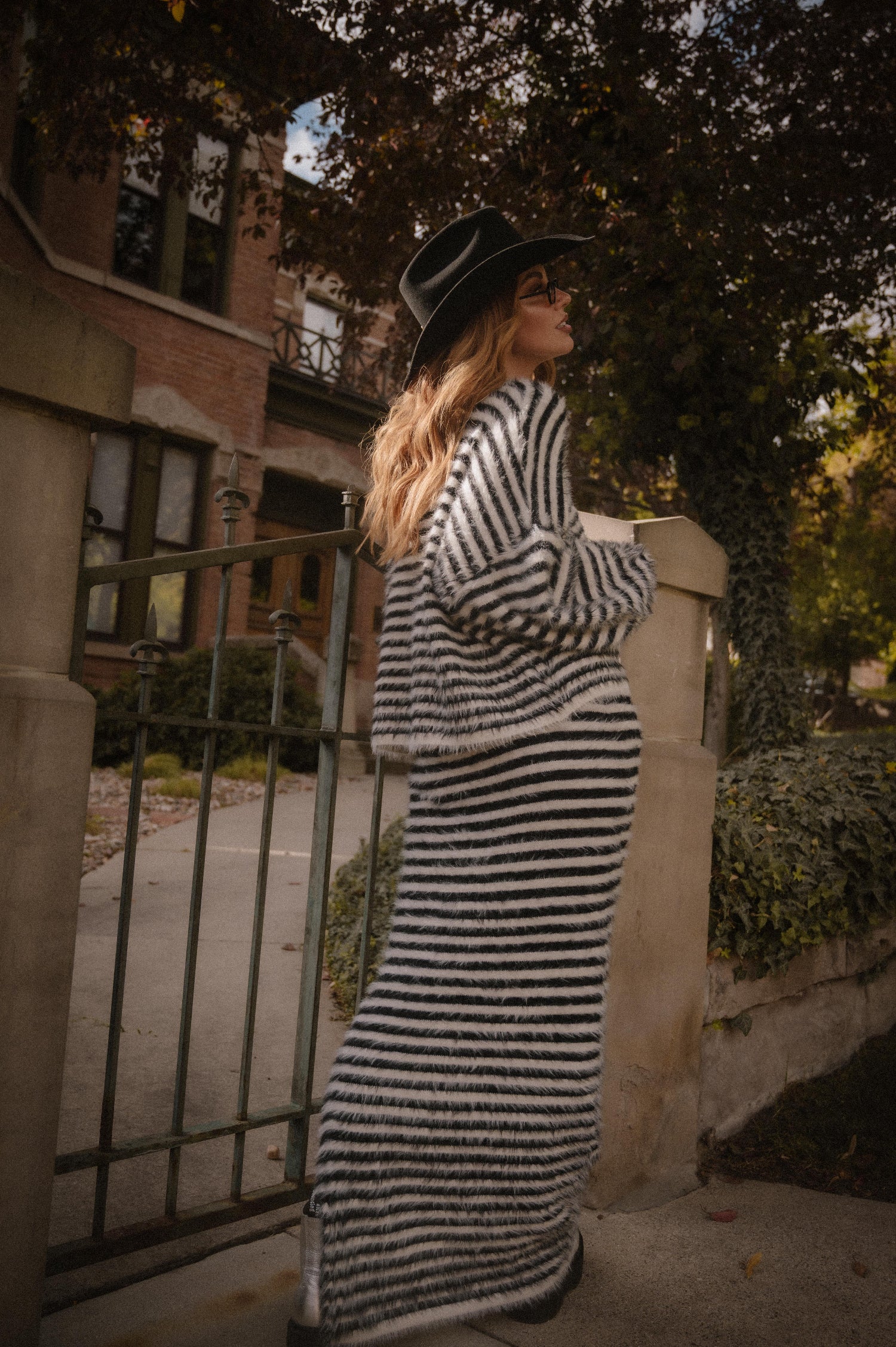 Woman in a black and white striped sweater and maxi skirt with fuzzy texture standing outdoors near a building.