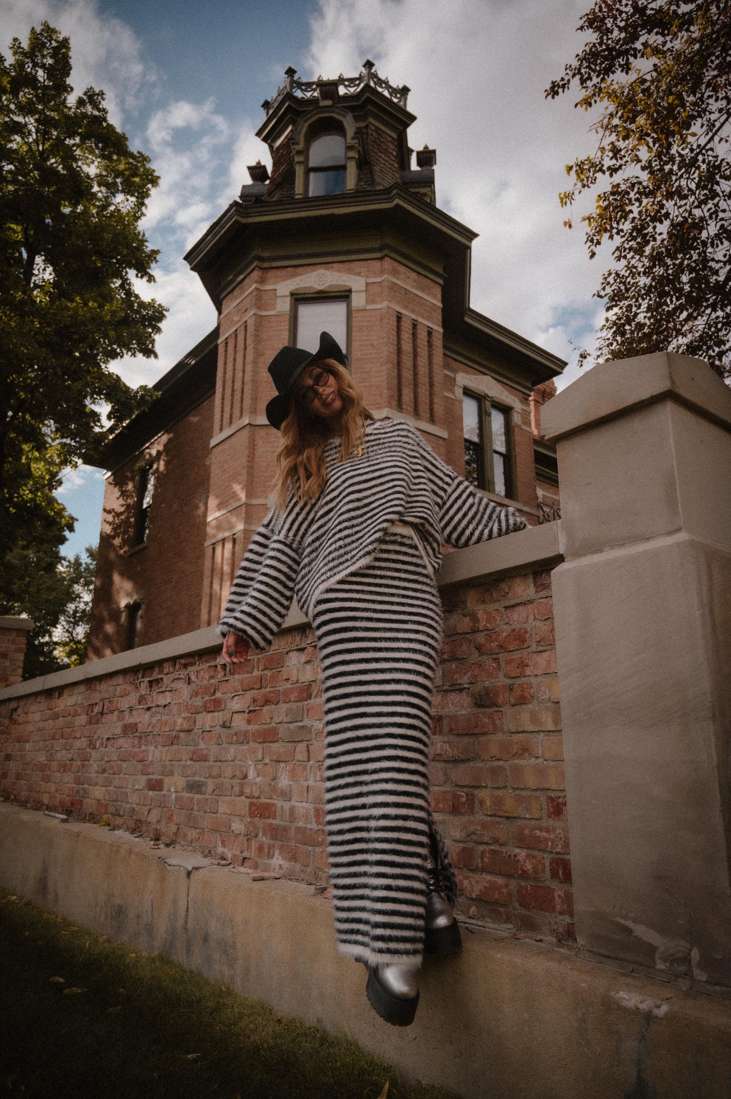 Person in striped sweater and skirt with fuzzy texture leaning against a brick wall with a historic building in the background