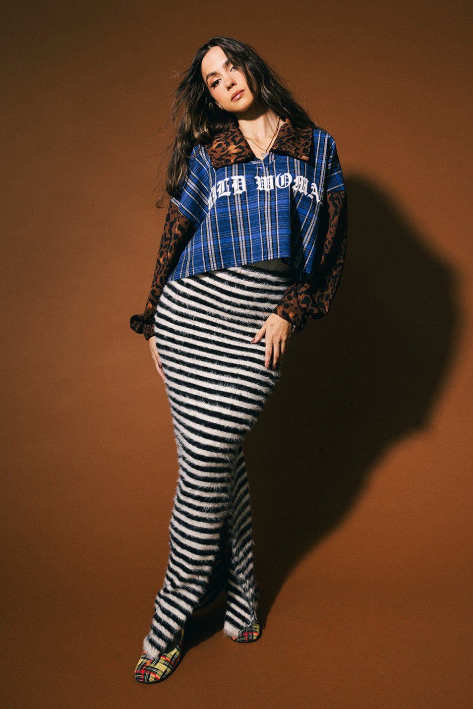 Person wearing a blue plaid shirt and black and white striped maxi skirt with fuzzy texture on a brown background