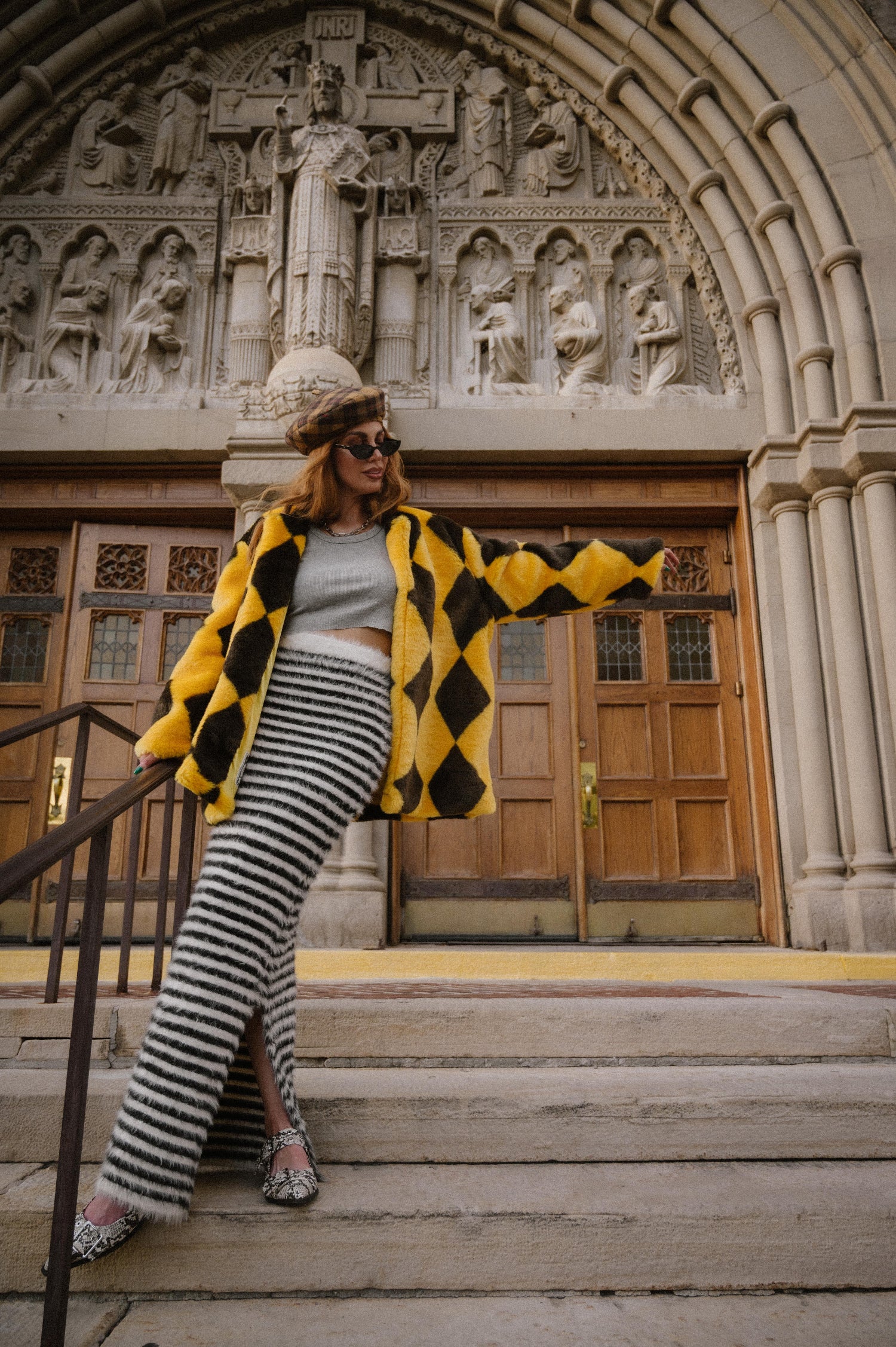 Person wearing a yellow and brown diamond faux fur coat and black and white striped maxi knit skirt with fuzzy texture and side slit in front of a cathedral entrance