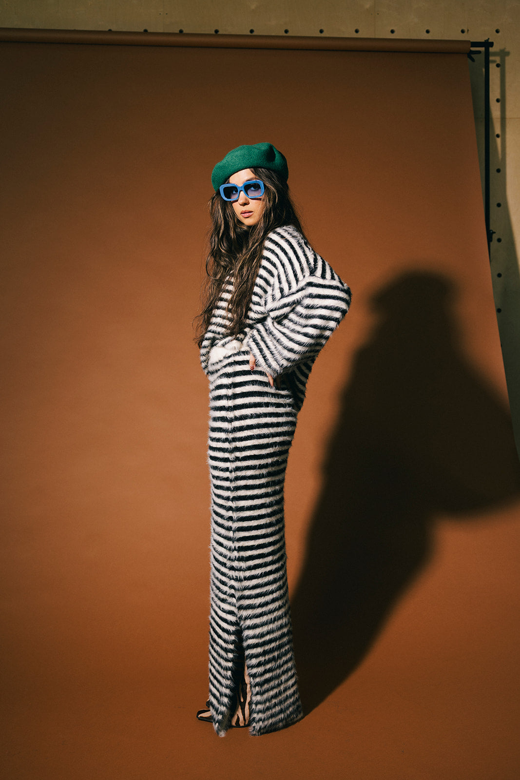 Woman wearing a black and white stripe sweater and maxi skirt with fuzzy texture against a brown background.