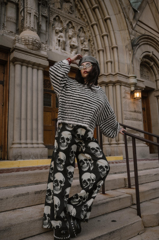Person wearing a black and white striped sweater and skull-patterned trousers standing on steps in front of a building.
