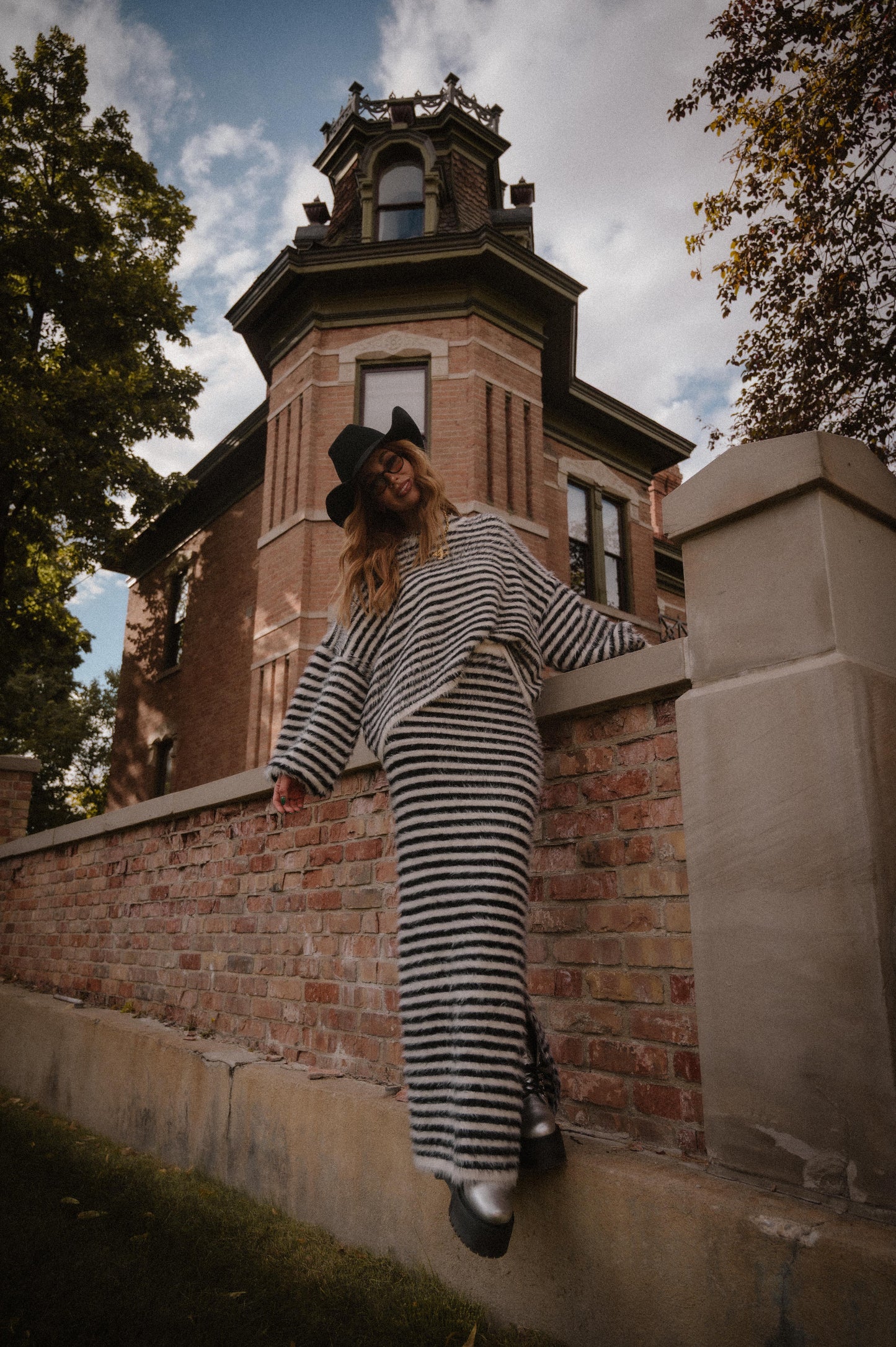 Person in striped sweater and skirt leaning against a brick wall with a historic building in the background