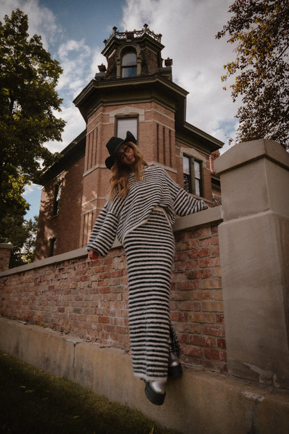 Person in striped sweater and skirt leaning against a brick wall with a historic building in the background