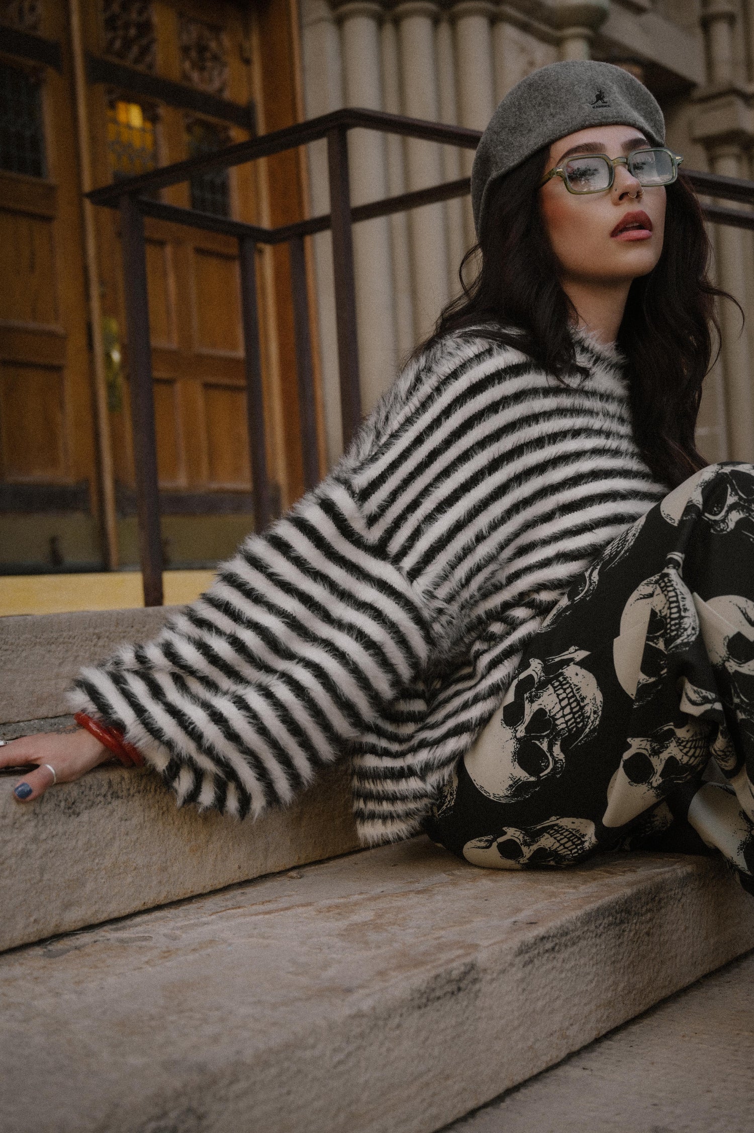Woman sitting on stone steps wearing a striped sweater and skull print trousers.