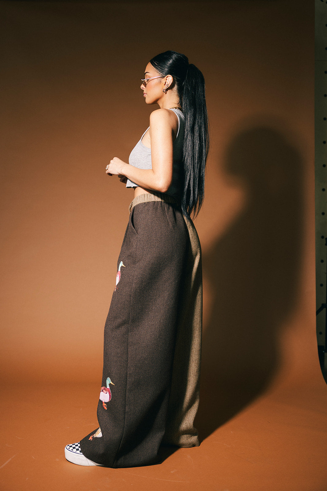 Woman wearing a sleeveless top and high-waisted pants against a brown background