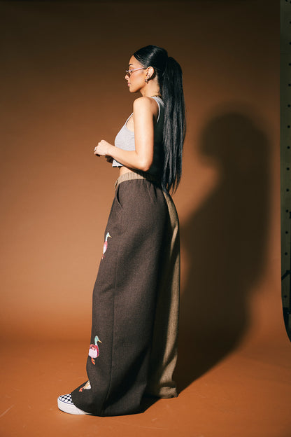 Woman wearing a sleeveless top and high-waisted pants against a brown background