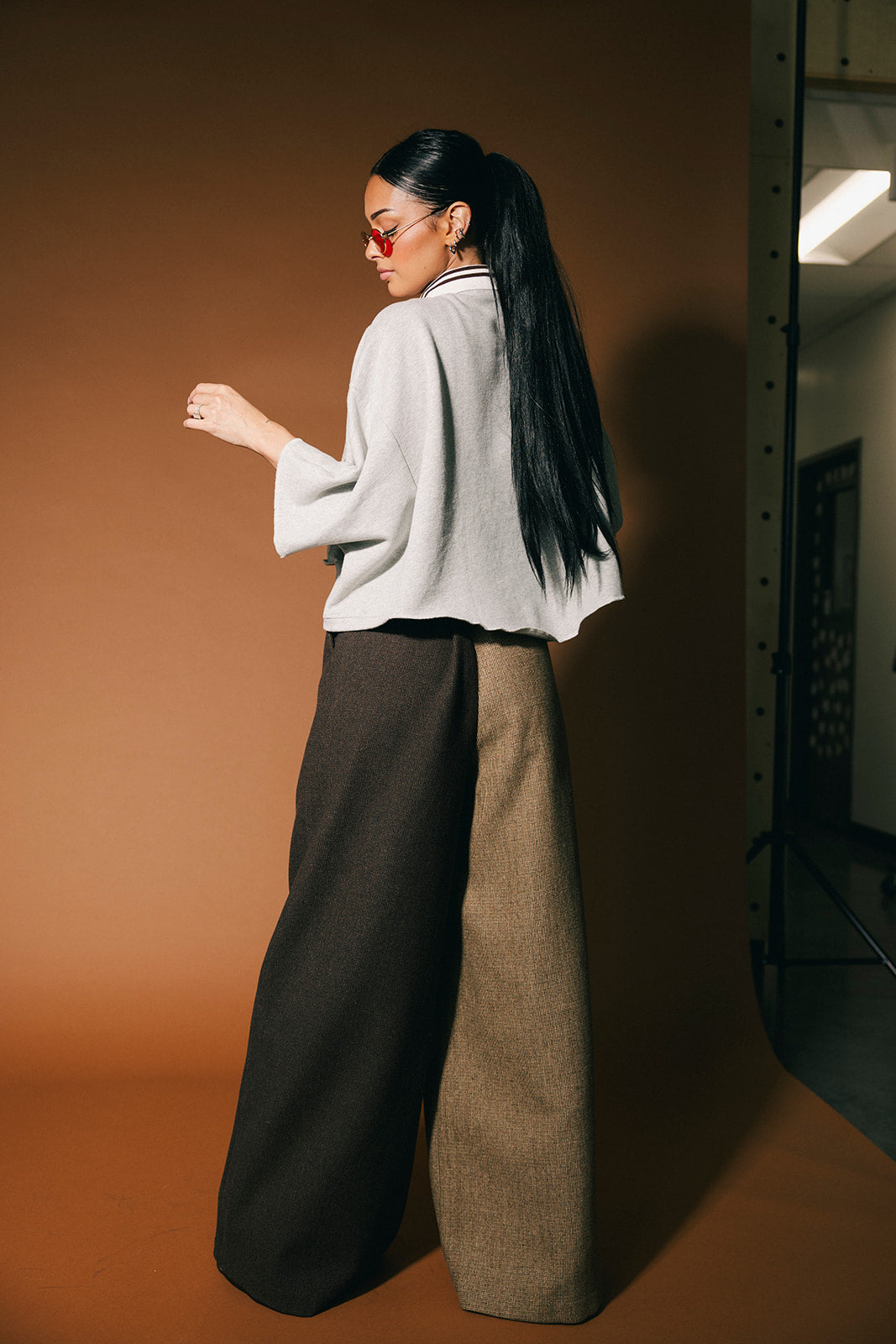 Woman wearing a grey polo and wide-leg pants against a brown background