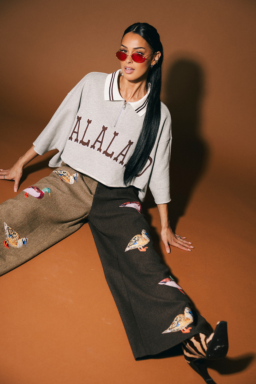 Woman wearing a 'LALALAND' shirt and pants with duck patches on a brown background