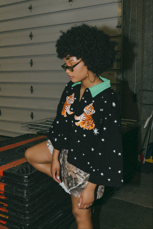 photo of girl wearing black cropped polo with green collar and white stars all over with baby tigers on the front and a baby tiger on the back words that say "made of stardust"