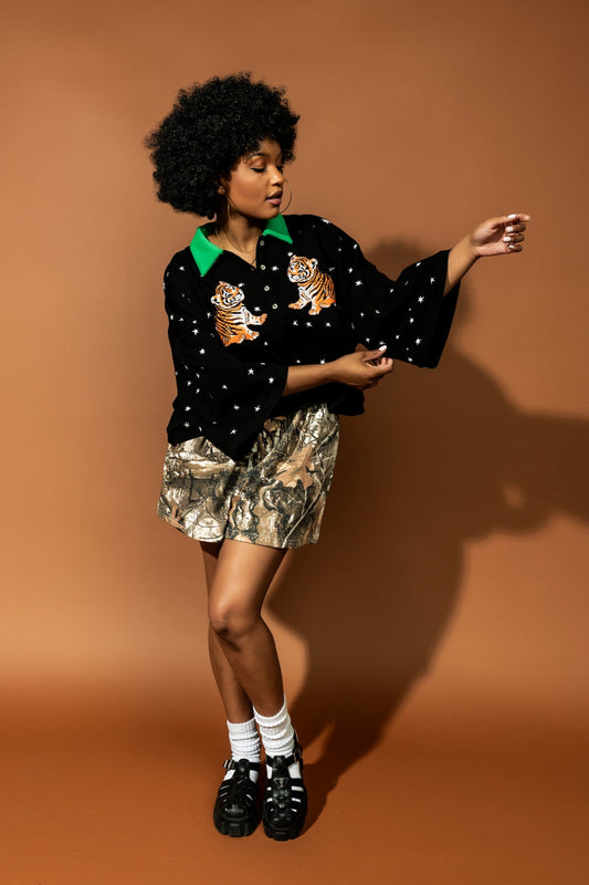 photo of girl wearing black cropped polo with green collar and white stars all over with baby tigers on the front and a baby tiger on the back words that say "made of stardust"