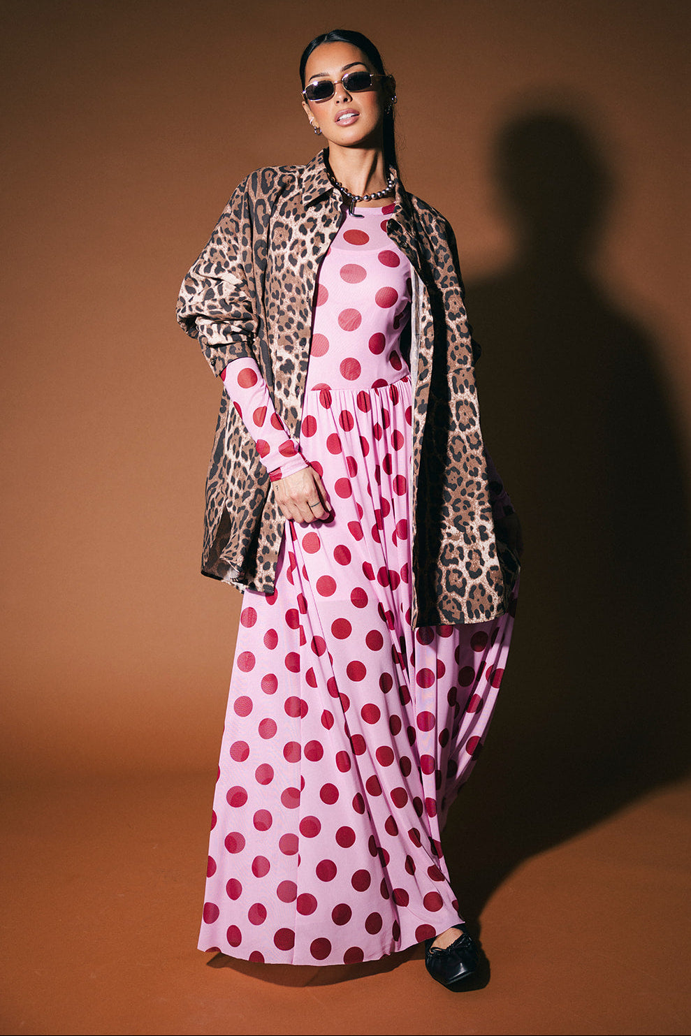 Woman wearing a leopard print button up over a pink polka dot dress on a brown background