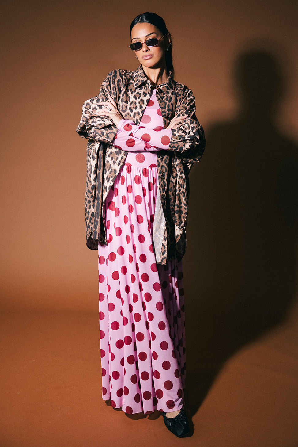 Woman wearing a pink polka dot dress with a leopard print button up against a brown background