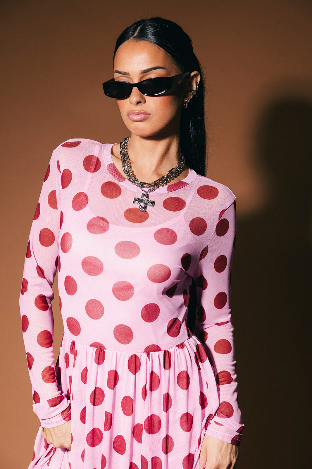 Woman wearing a pink dress with maroon polka dots against a brown background