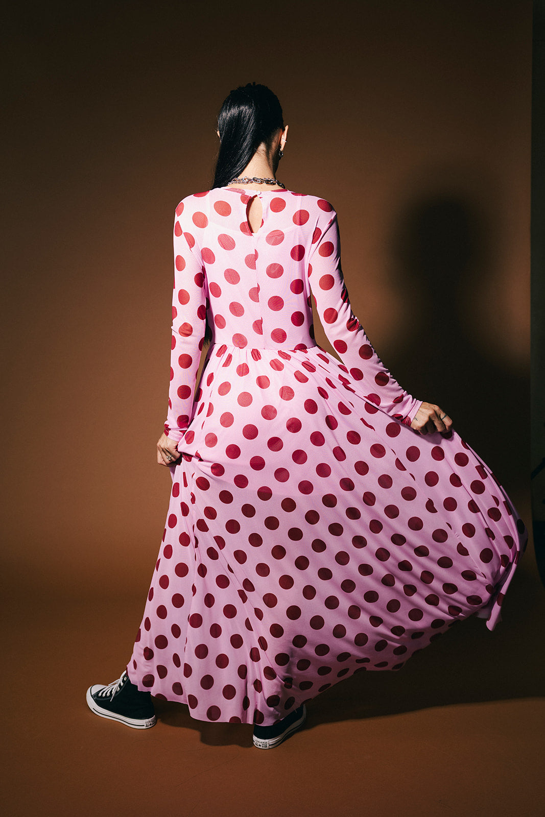 Person wearing a long pink polka dot dress on a brown background