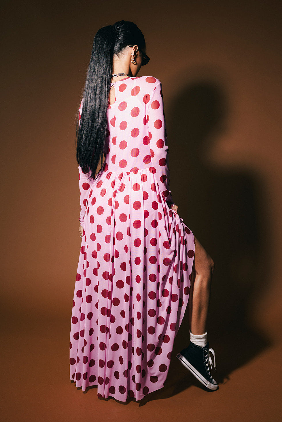 Person wearing a pink dress with maroon polka dots on a brown background