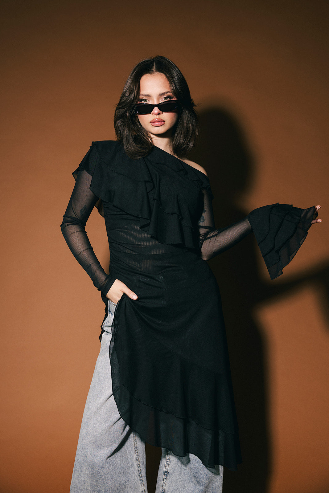 Woman wearing a black sheer tunic against a brown background