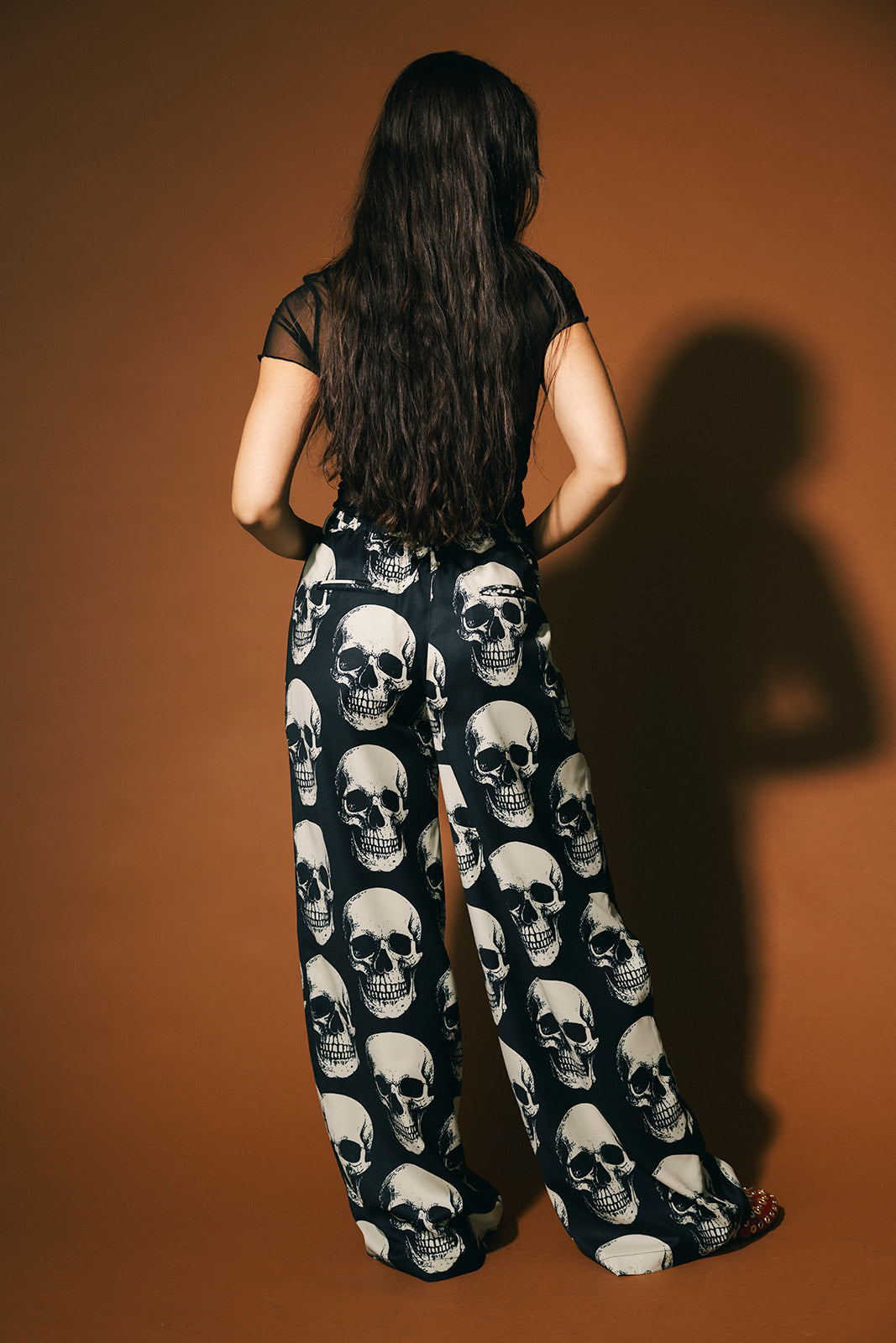 Person wearing a black top and skull-patterned trousers on a brown background