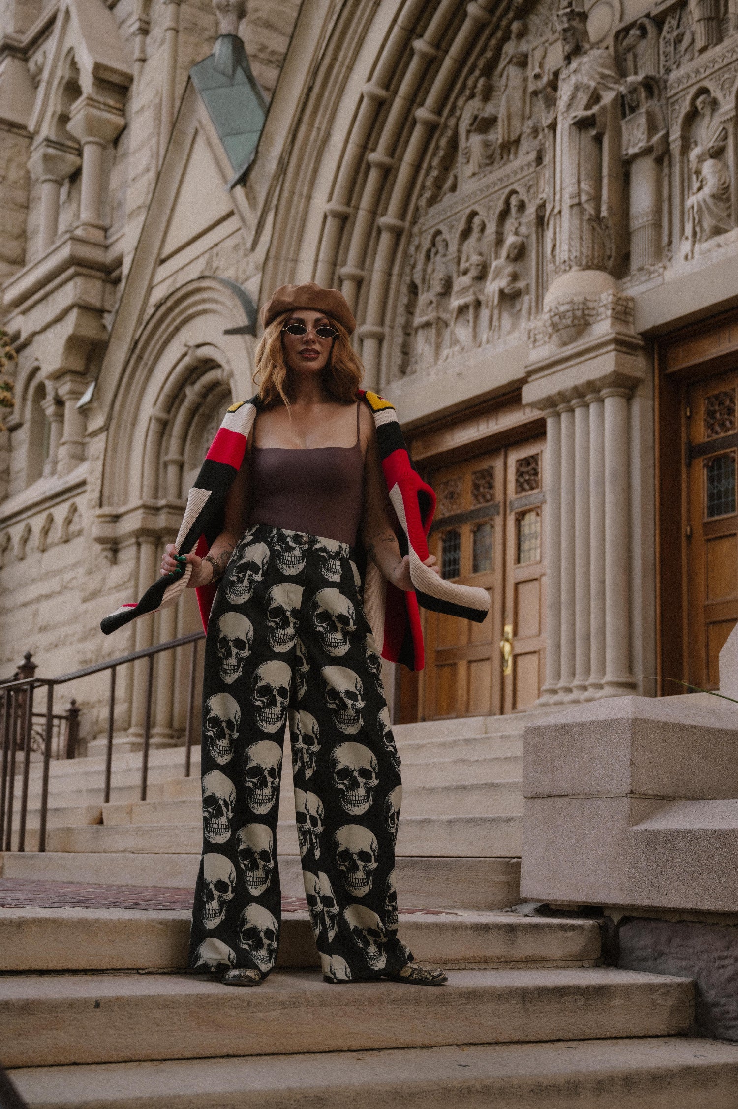 Person wearing trousers with skull-pattern in front of a large building.