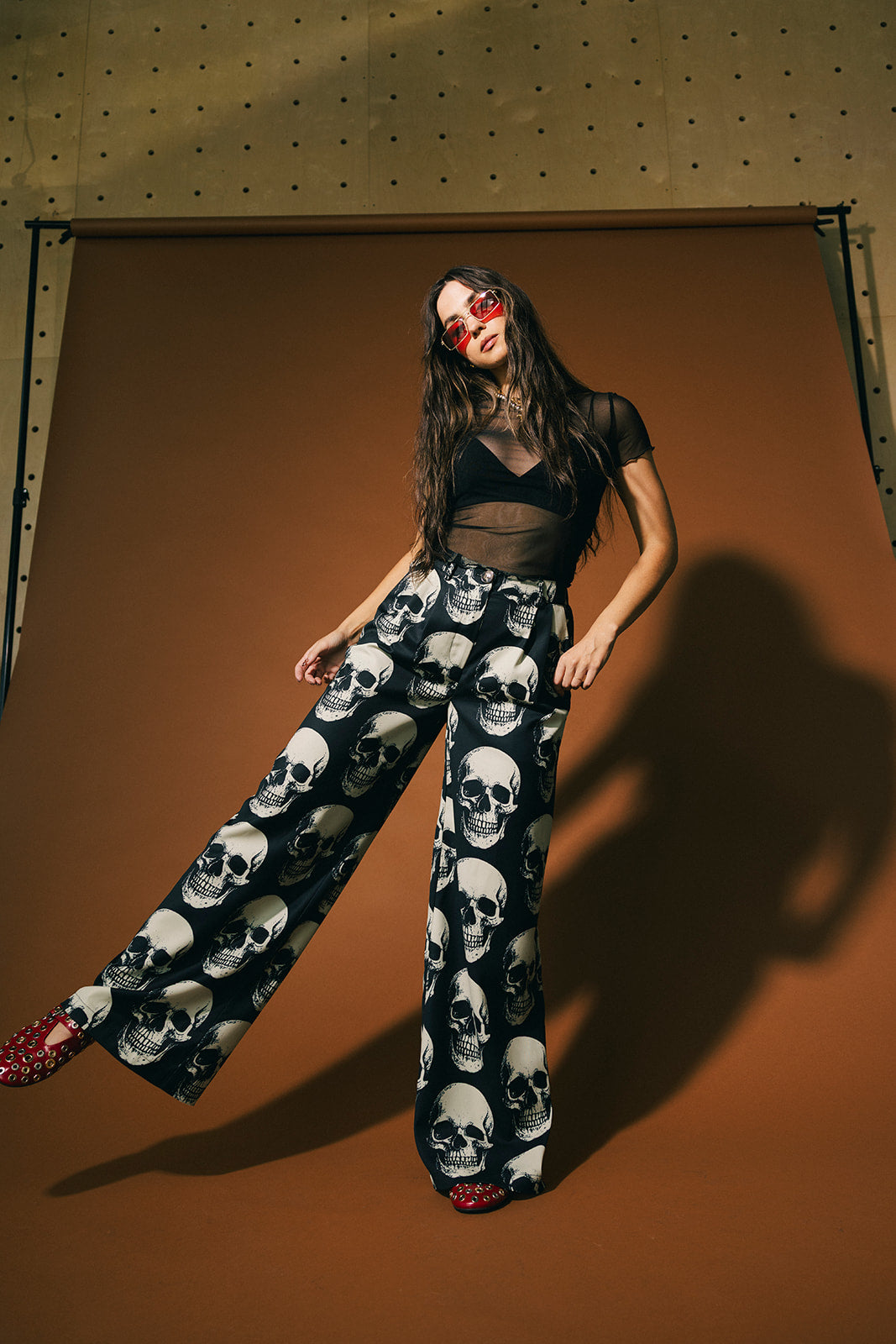 Woman wearing a black top and skull-patterned trousers against a brown background