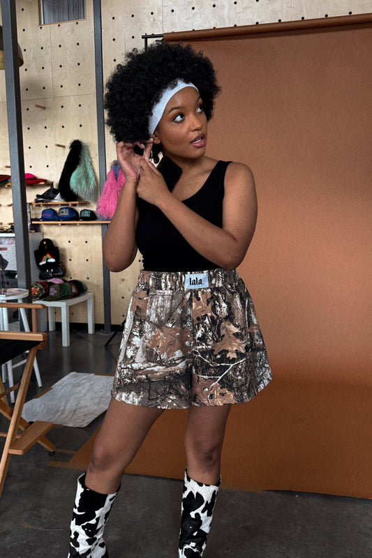 photo of girl wearing real tree camo sweat boxer shorts with an elastic waistband, side pockets, three faux button fly, and white satin label that says "lala"