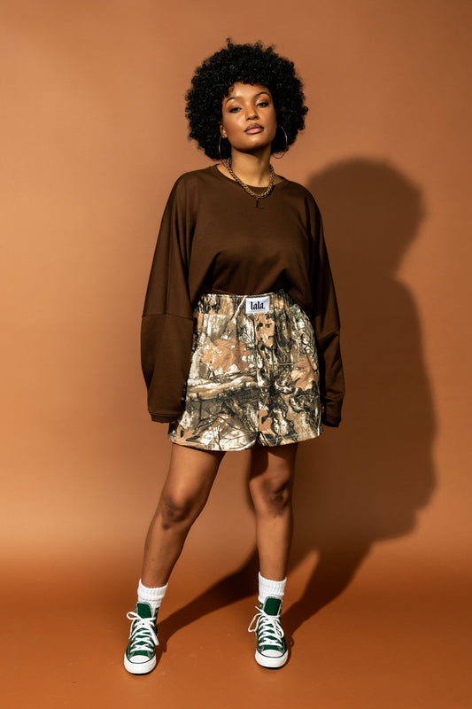 photo of girl wearing real tree camo sweat boxer shorts with an elastic waistband, side pockets, three faux button fly, and white satin label that says "lala"