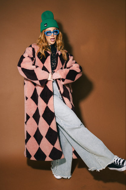 Person wearing a pink and maroon harlequin long faux fur coat on a brown background