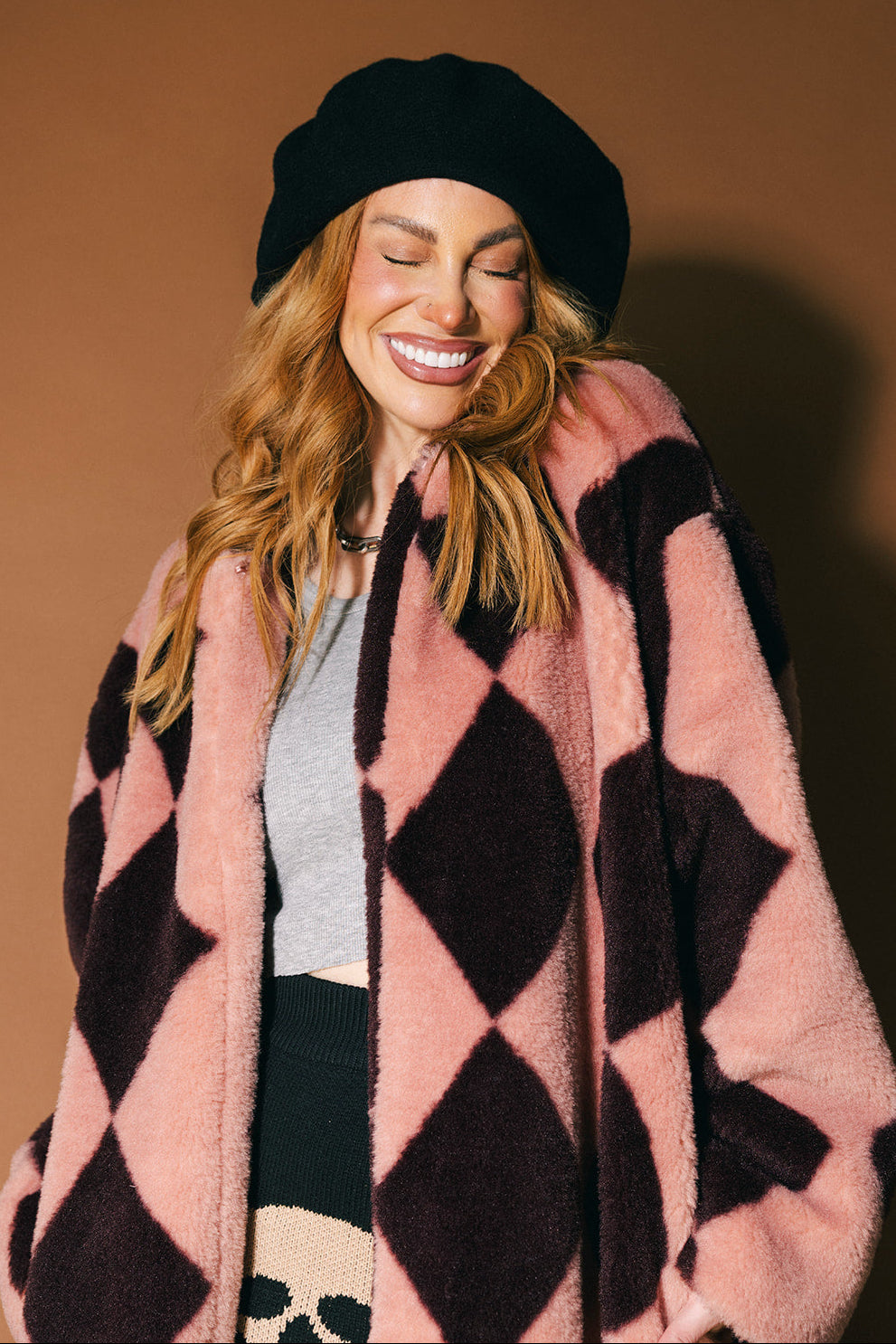Person wearing a pink and maroon harlequin long faux fur coat on a brown background