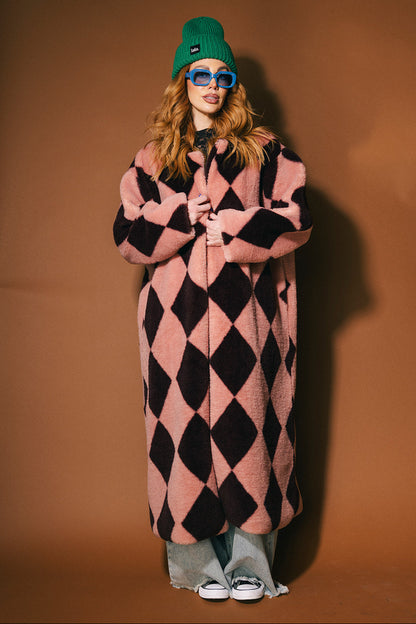 Person wearing a pink and maroon harlequin long faux fur coat on a brown background
