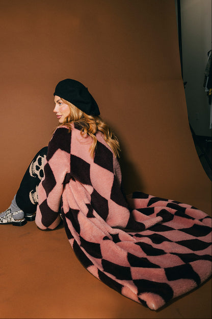 Person wearing a pink and maroon harlequin long faux fur coat on a brown background