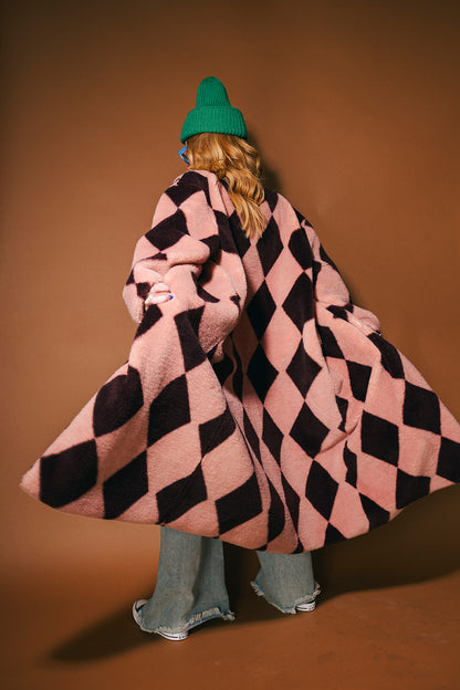 Person wearing a pink and maroon harlequin long faux fur coat on a brown background