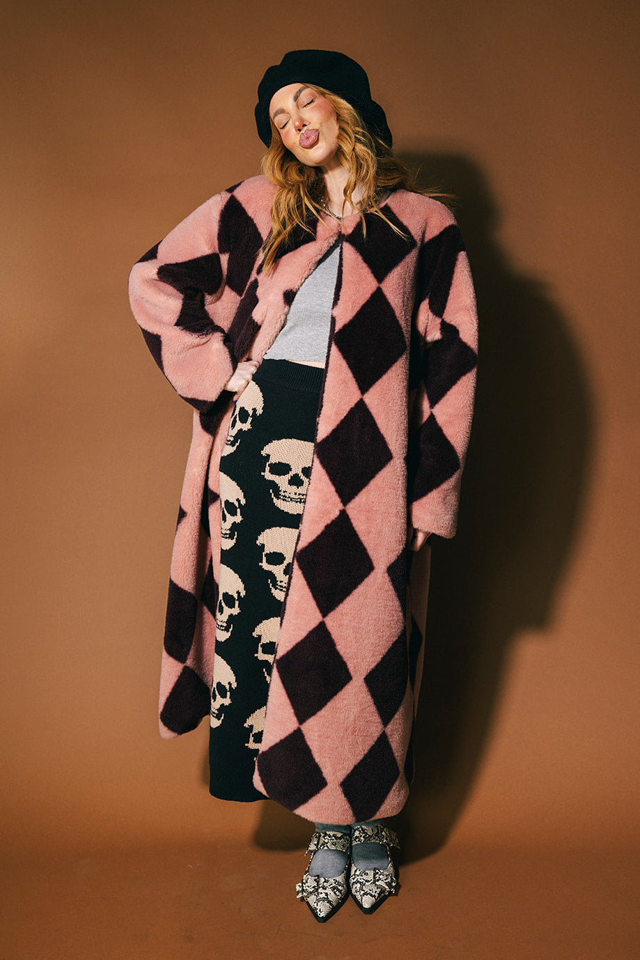 Person wearing a pink and maroon harlequin long faux fur coat on a brown background