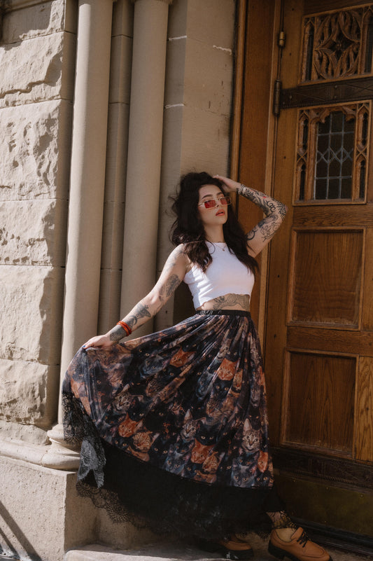 Woman in a cat pattern skirt and white top leaning against a stone building with a wooden door.