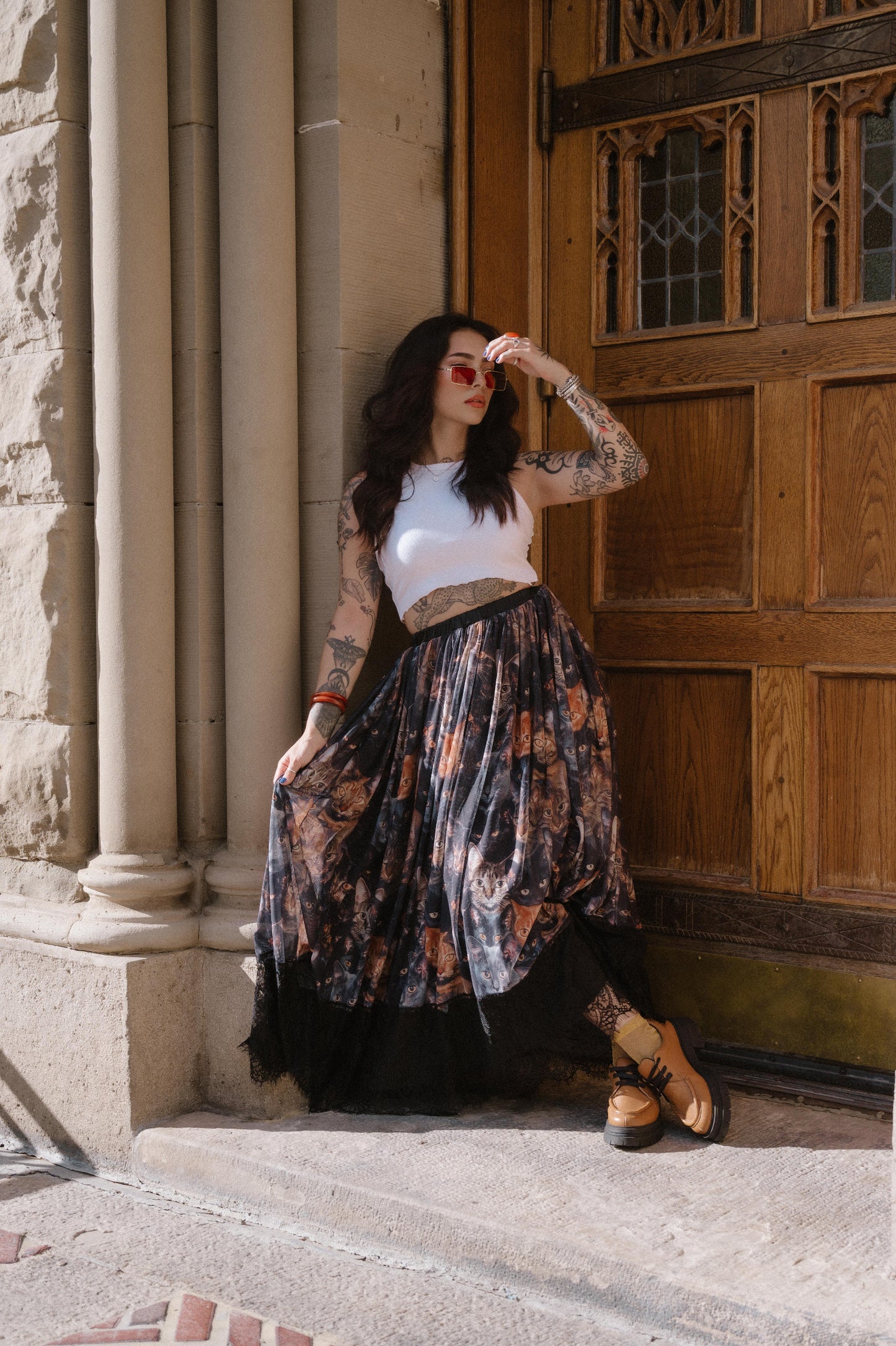 Woman standing in front of a wooden door with stone columns wearing a cat pattern mesh skirt with lace hem.