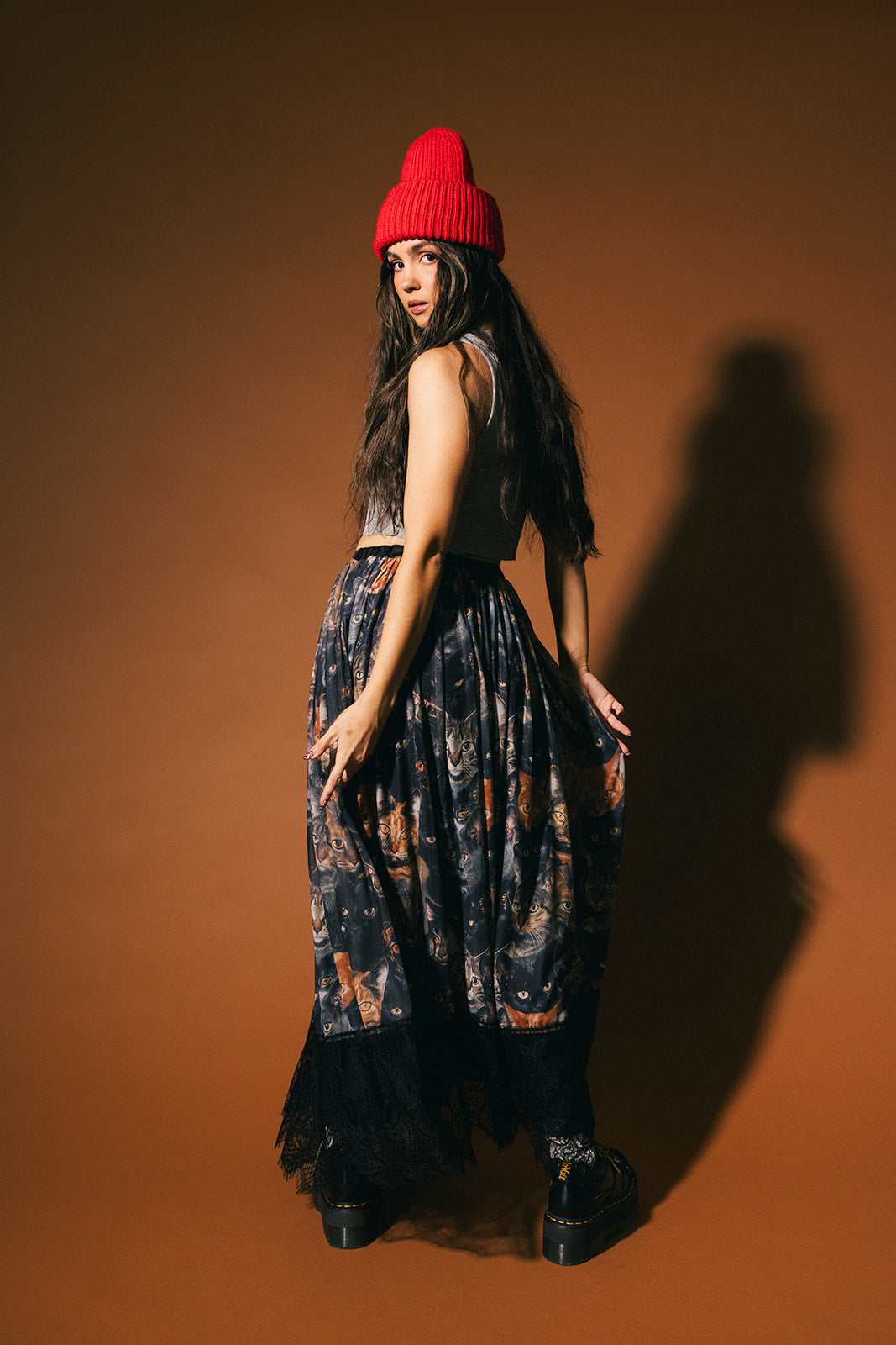 Woman wearing a red beanie and cat patterned mesh maxi skirt with lace hem against a brown background