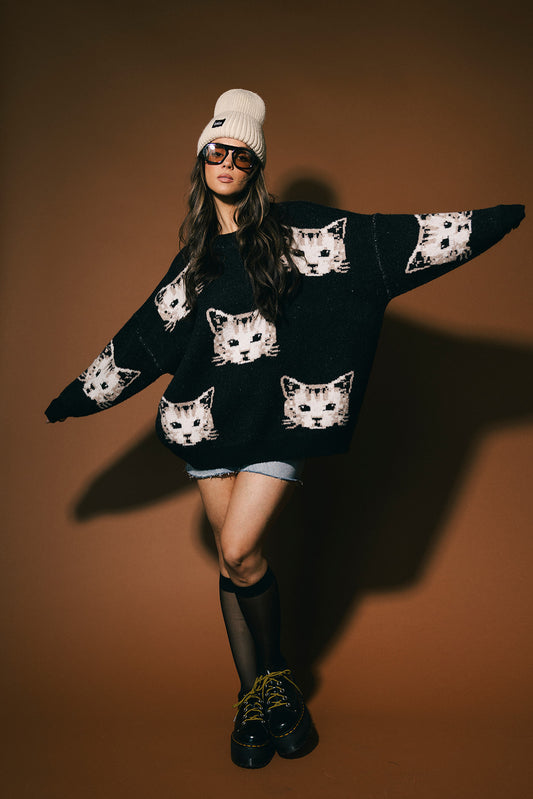 Person wearing a black sweater with cat heads against a brown background
