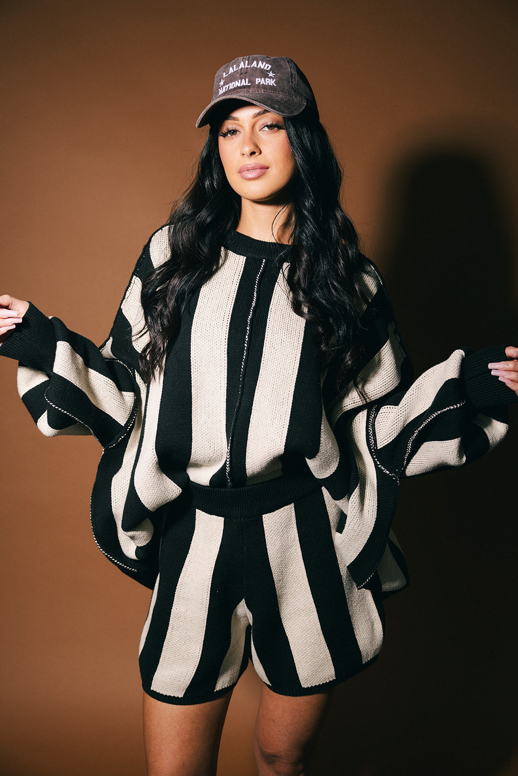 Woman wearing a black and white striped outfit with a cap against a brown background