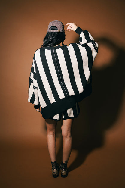 Person wearing a black and white striped sweater with a cap on a brown background