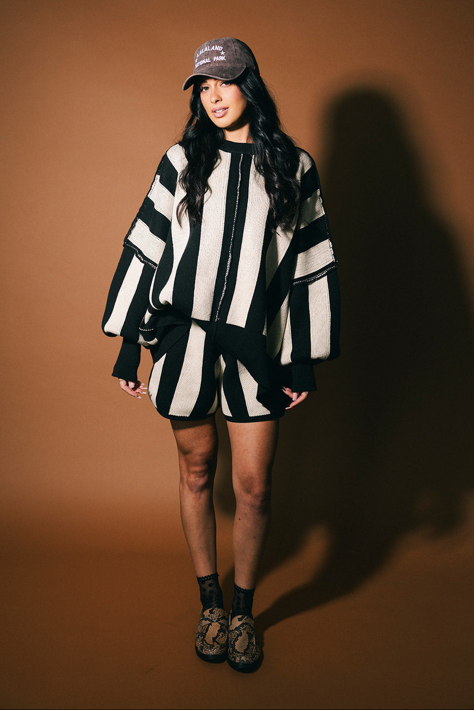 Person wearing a black and white striped outfit with a cap on a brown background