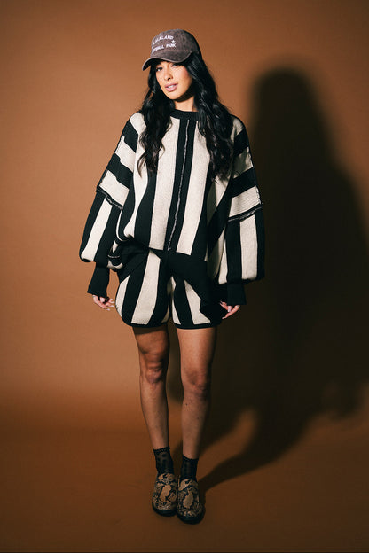 Person wearing a black and white striped outfit with a cap on a brown background