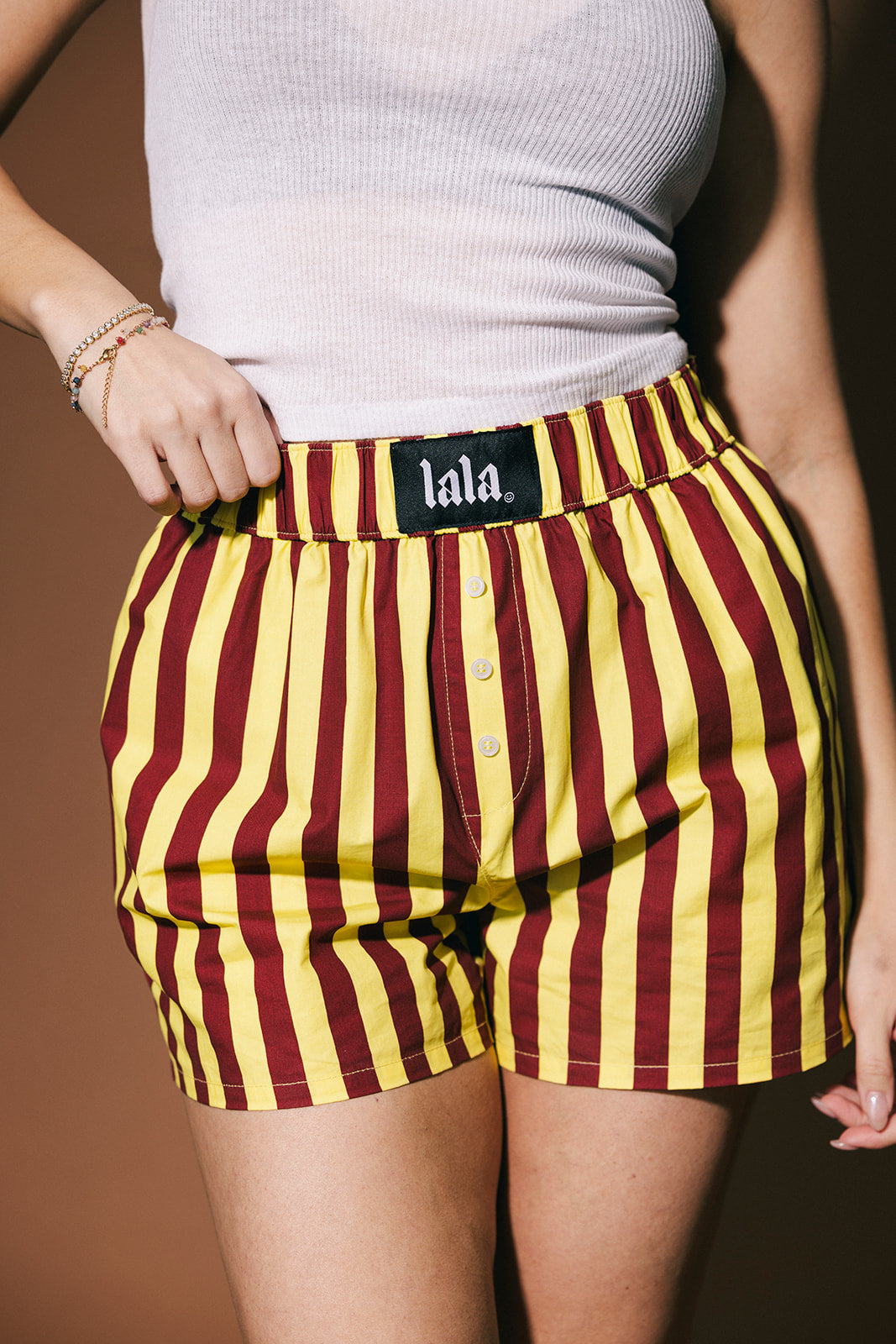 Person wearing maroon and yellow striped shorts with 'lala' brand label on a brown background