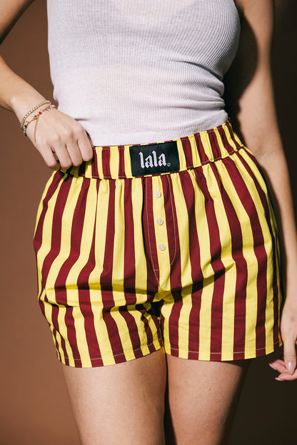 Person wearing maroon and yellow striped shorts with 'lala' brand label on a brown background
