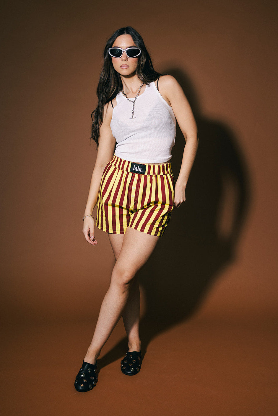 Woman wearing a white sleeveless top and red and yellow striped shorts against a brown background